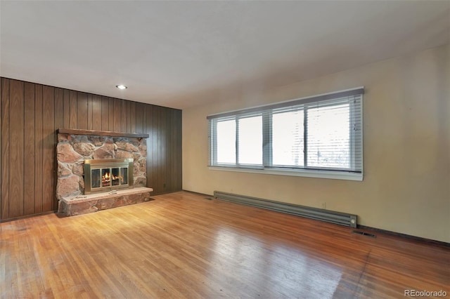 unfurnished living room with a fireplace, light hardwood / wood-style flooring, baseboard heating, and wooden walls