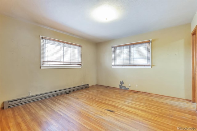 empty room featuring light hardwood / wood-style floors, a healthy amount of sunlight, and a baseboard heating unit