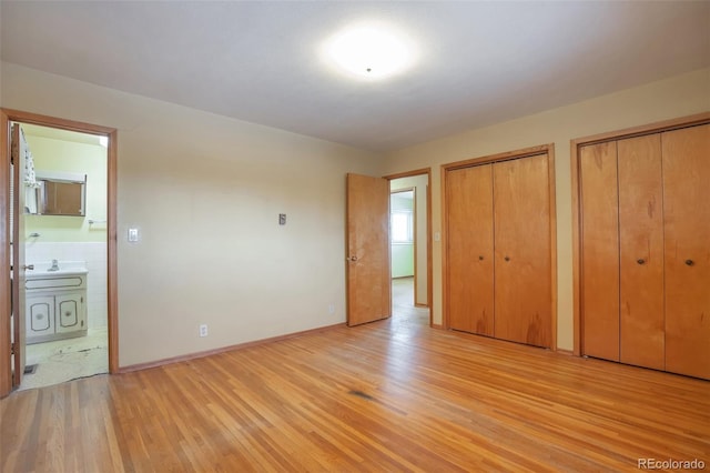 unfurnished bedroom with two closets, ensuite bathroom, and light hardwood / wood-style flooring