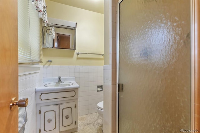 bathroom featuring vanity, toilet, a shower with door, and tile walls