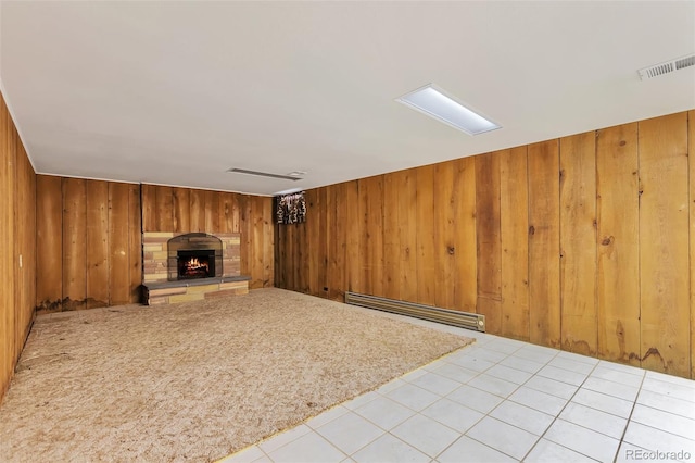 unfurnished living room featuring wood walls, light tile patterned floors, a fireplace, and a baseboard heating unit