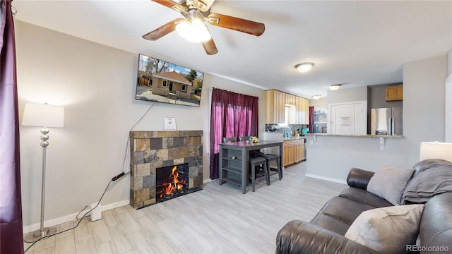 living room featuring light wood-type flooring, ceiling fan, and a stone fireplace