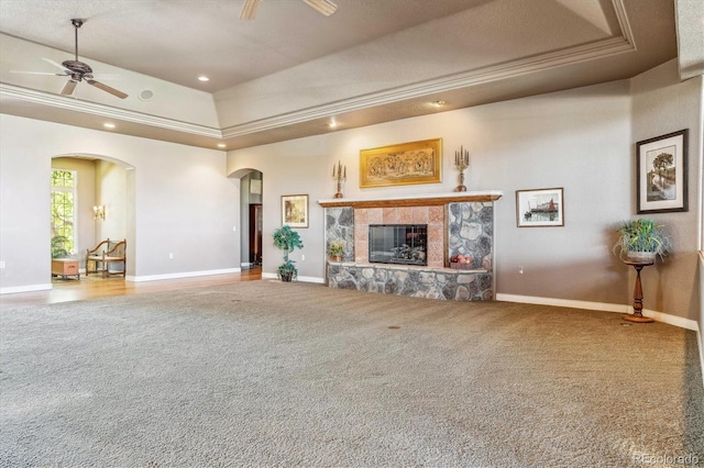 unfurnished living room featuring a tray ceiling, a stone fireplace, ceiling fan, and carpet