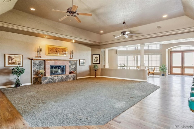 living room with light hardwood / wood-style floors, a stone fireplace, ceiling fan, and a tray ceiling