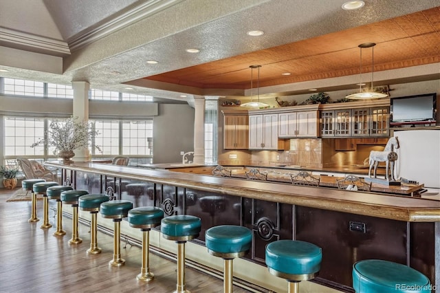 bar featuring wood-type flooring, a tray ceiling, decorative backsplash, and decorative light fixtures