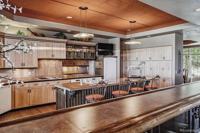 kitchen featuring dark hardwood / wood-style flooring, a kitchen breakfast bar, hanging light fixtures, decorative backsplash, and a raised ceiling