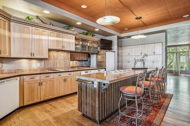 kitchen with pendant lighting, white appliances, a breakfast bar, a kitchen island, and a raised ceiling