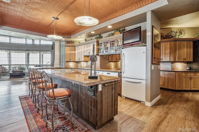 kitchen with hanging light fixtures, a kitchen island, white refrigerator, a tray ceiling, and a kitchen bar