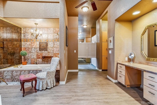 bathroom with ceiling fan with notable chandelier, hardwood / wood-style floors, vanity, tiled tub, and a textured ceiling