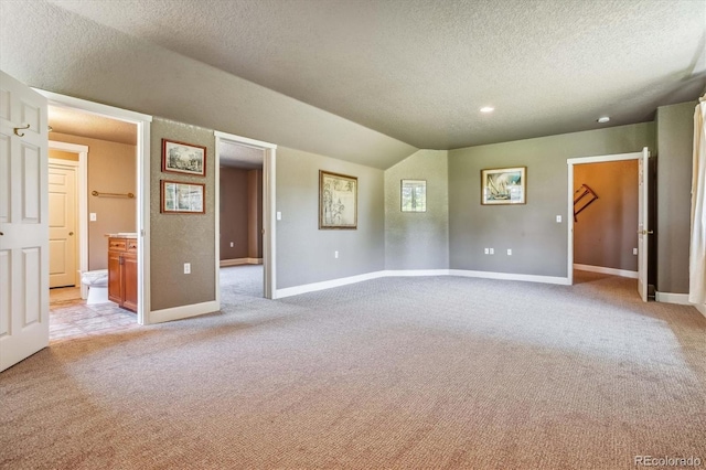 unfurnished room featuring lofted ceiling, light colored carpet, and a textured ceiling