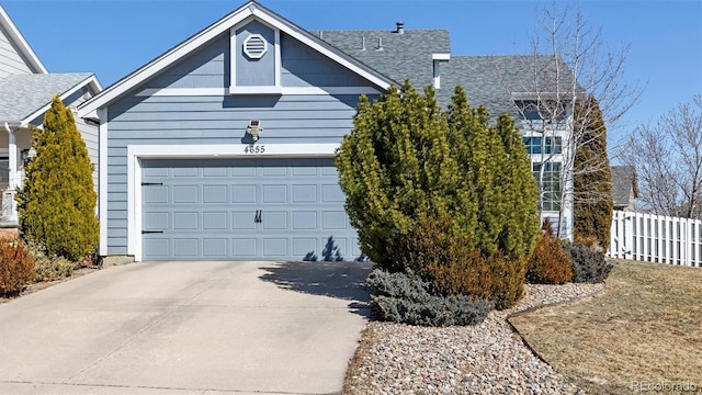 view of front of house with a shingled roof, concrete driveway, an attached garage, and fence