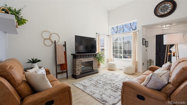 living room with a stone fireplace, a high ceiling, wood finished floors, and baseboards