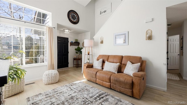 living room featuring a high ceiling, wood finished floors, visible vents, and baseboards