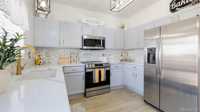 kitchen featuring a sink, stainless steel appliances, light stone countertops, and backsplash