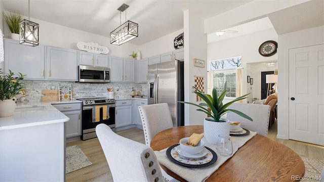 kitchen with tasteful backsplash, light wood-style floors, appliances with stainless steel finishes, light countertops, and hanging light fixtures