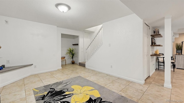 tiled spare room featuring a textured ceiling, stairs, and baseboards