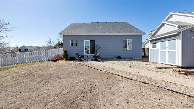 back of property with a storage shed, an outdoor structure, fence, and a shingled roof