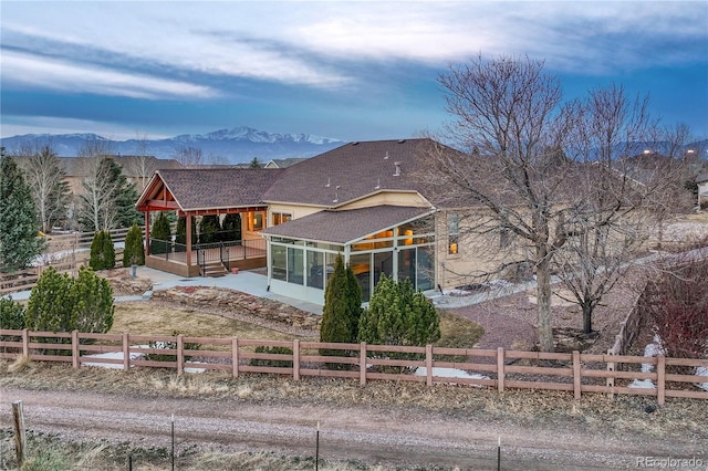 back of property with a mountain view, roof with shingles, fence private yard, and a sunroom