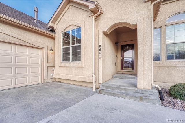 view of exterior entry featuring stucco siding, a garage, and driveway