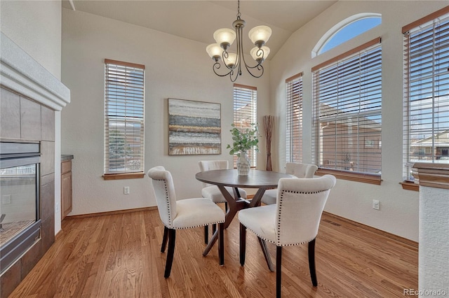 dining room featuring baseboards, a fireplace, vaulted ceiling, light wood-style floors, and a chandelier