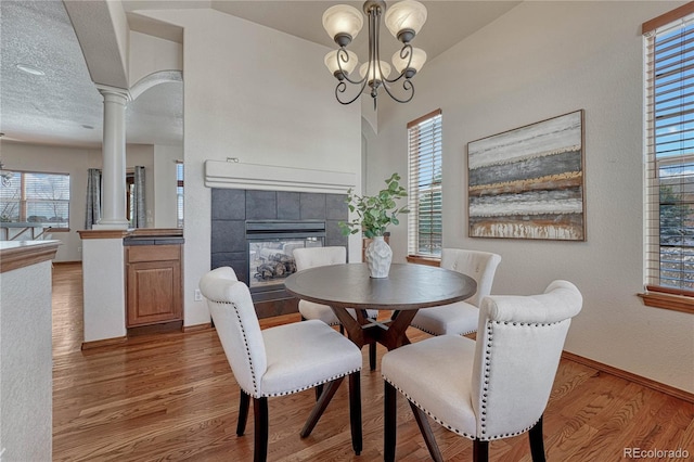 dining space with a tiled fireplace, wood finished floors, decorative columns, baseboards, and a chandelier