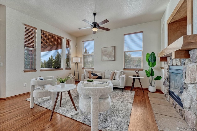 living room with a healthy amount of sunlight, a fireplace, ceiling fan, and wood finished floors