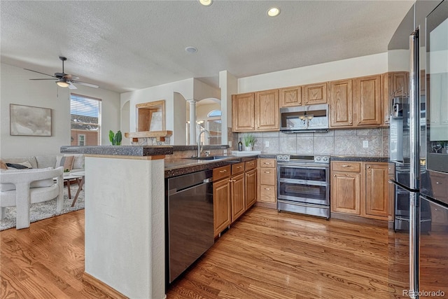 kitchen with ceiling fan, open floor plan, appliances with stainless steel finishes, arched walkways, and a sink