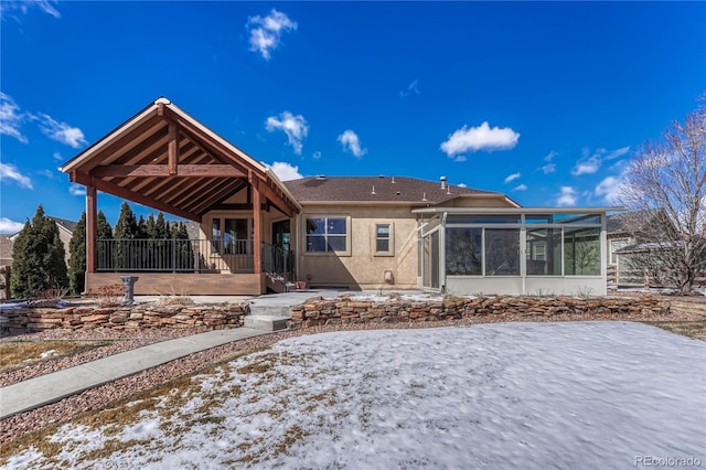 snow covered back of property featuring stucco siding and a sunroom