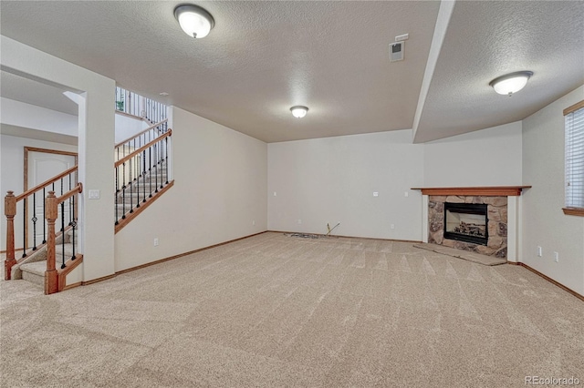 unfurnished living room with a textured ceiling, a stone fireplace, carpet flooring, baseboards, and stairs