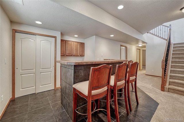 bar featuring stairway, recessed lighting, a textured ceiling, and bar area