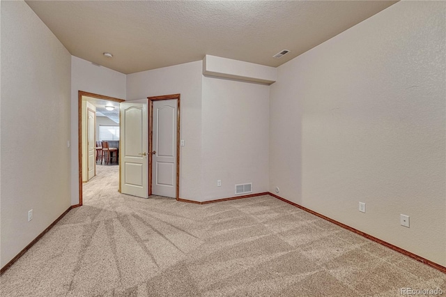 empty room featuring visible vents, baseboards, light colored carpet, and a textured ceiling