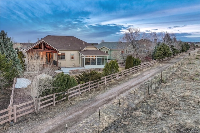 rear view of property featuring fence, roof with shingles, stucco siding, a sunroom, and a patio area