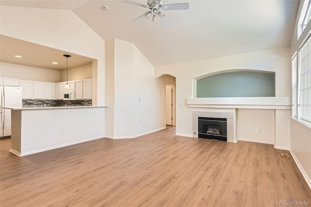unfurnished living room with a ceiling fan, high vaulted ceiling, a tiled fireplace, healthy amount of natural light, and light wood-style floors