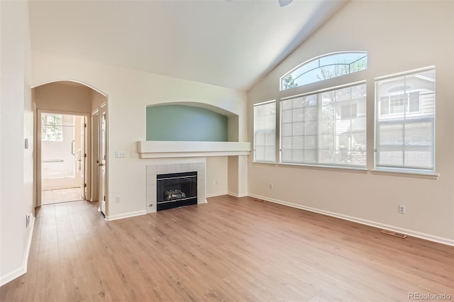 unfurnished living room with wood finished floors, plenty of natural light, a tile fireplace, baseboards, and high vaulted ceiling