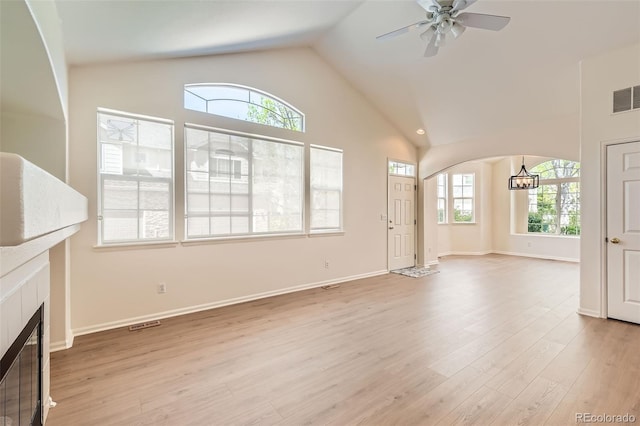 unfurnished living room featuring healthy amount of natural light, a tiled fireplace, light wood-style flooring, and high vaulted ceiling