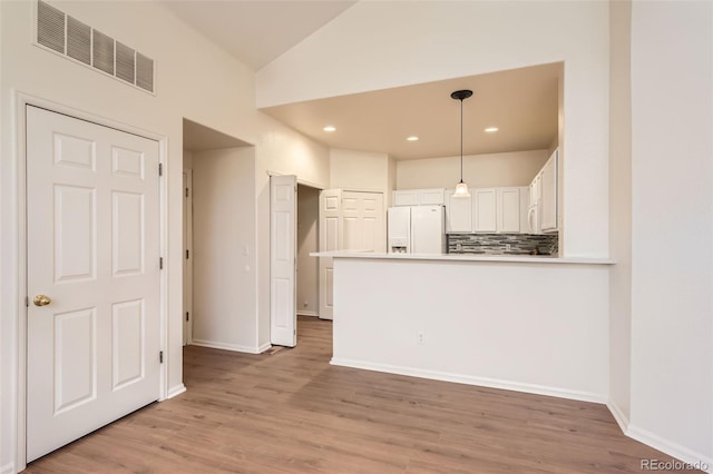 kitchen with white appliances, tasteful backsplash, white cabinets, vaulted ceiling, and light wood-type flooring