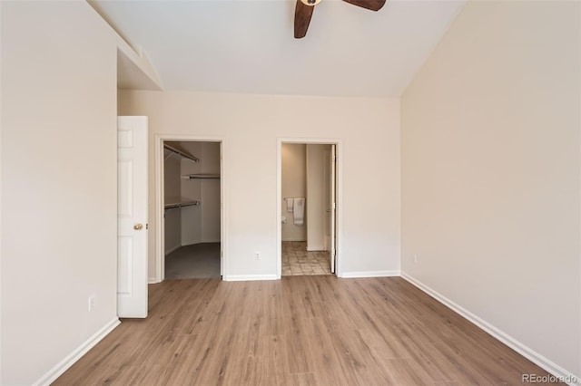 unfurnished bedroom featuring a walk in closet, light wood-style flooring, baseboards, and a closet