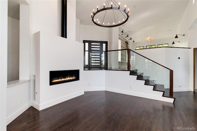 unfurnished living room with dark wood-type flooring, a notable chandelier, rail lighting, and a towering ceiling