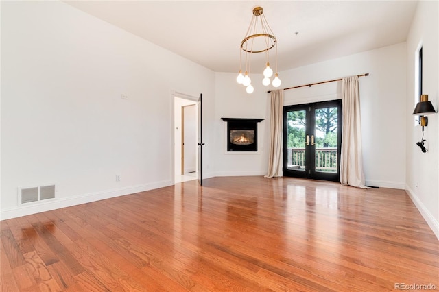 spare room featuring light wood-type flooring, a notable chandelier, and french doors