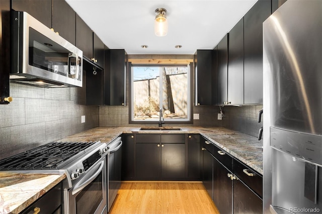 kitchen with light wood finished floors, tasteful backsplash, appliances with stainless steel finishes, light stone counters, and a sink