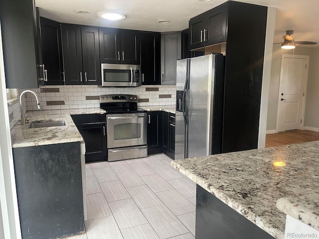 kitchen with light stone countertops, stainless steel appliances, sink, backsplash, and ceiling fan