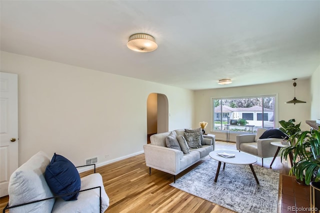 living room featuring light wood-style floors, visible vents, baseboards, and arched walkways
