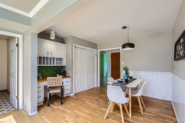 dining room featuring built in desk, light wood-style flooring, and a wainscoted wall