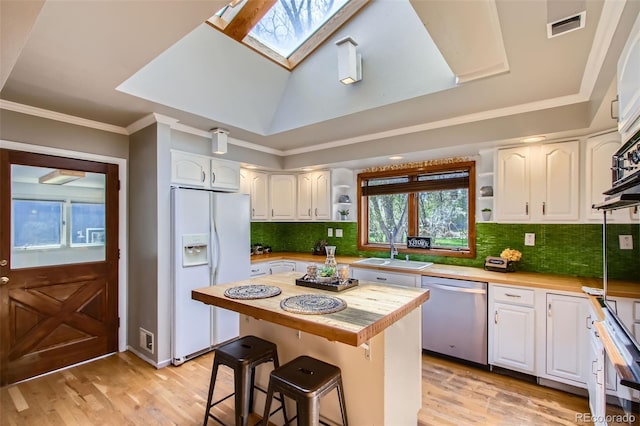 kitchen with a sink, a skylight, dishwasher, white cabinetry, and white refrigerator with ice dispenser