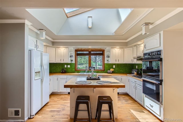 kitchen with a breakfast bar area, white refrigerator with ice dispenser, white cabinetry, dobule oven black, and light countertops