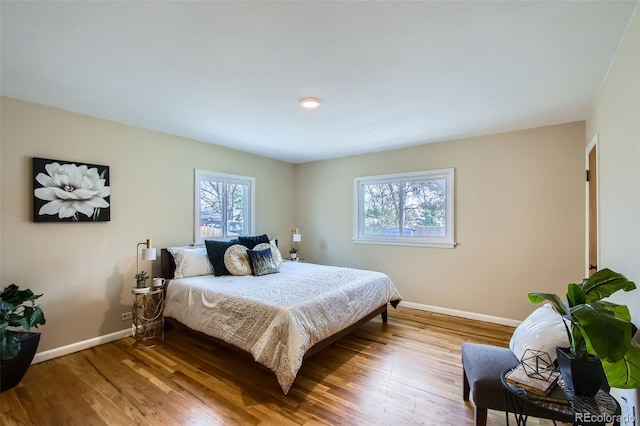 bedroom with multiple windows, wood finished floors, and baseboards