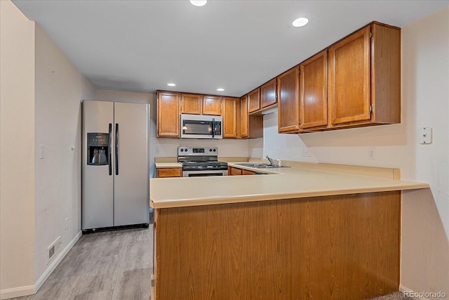 8438 Everett Way Unit B, Arvada, CO 80005 - kitchen featuring appliances with stainless steel finishes, brown cabinets, light wood-type flooring, a peninsula, and light countertops
