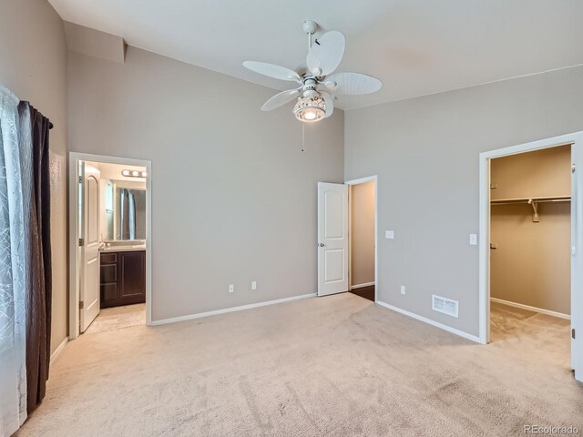 unfurnished bedroom with a spacious closet, a closet, a high ceiling, ceiling fan, and light colored carpet