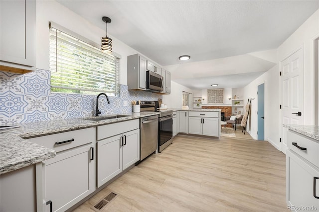 13275 W 63rd Pl, Arvada, CO 80004 - kitchen featuring appliances with stainless steel finishes, a peninsula, light wood finished floors, decorative backsplash, and light stone countertops