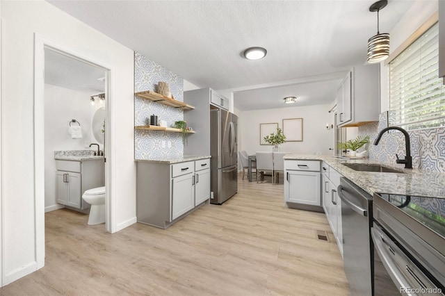 13275 W 63rd Pl, Arvada, CO 80004 - kitchen featuring appliances with stainless steel finishes, light wood-style floors, open shelves, light stone counters, and a textured ceiling